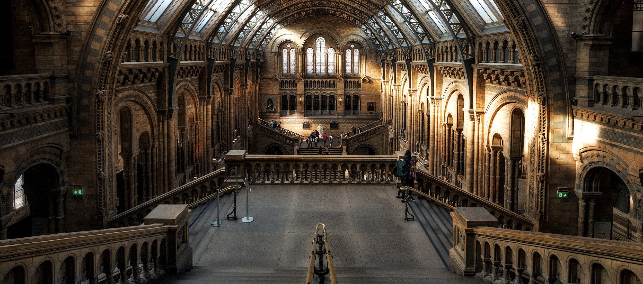 The interior of this grand, historic building, often featured in the tour itinerary, boasts arched windows and ornate stonework. A majestic staircase leads to a balcony, with sunlight streaming through the upper windows to highlight the exquisite architectural details on the walls and ceiling.